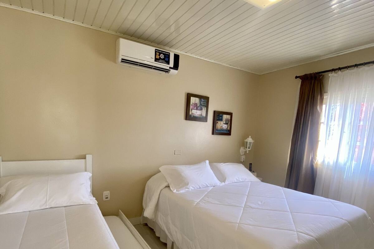 A hotel room with two beds, a ceiling fan, an air conditioning unit, and a window with curtains.