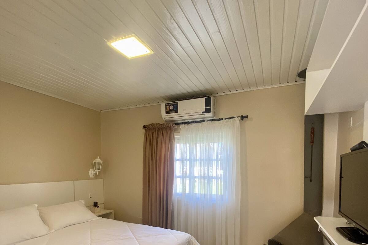 A hotel room with a large bed, an air conditioning unit, a television, and a small desk.