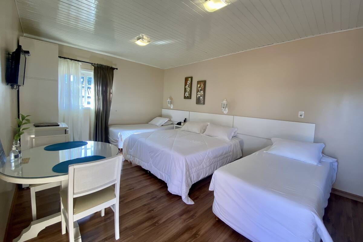 A hotel room with two single beds, a small table with chairs, a TV mounted on the wall, and a window with curtains.