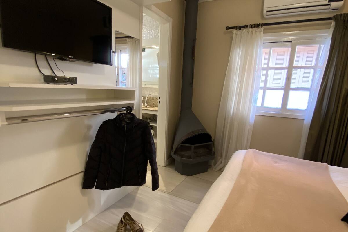 A hotel room with a bed, a TV mounted on the wall, a heater, and a window with curtains.