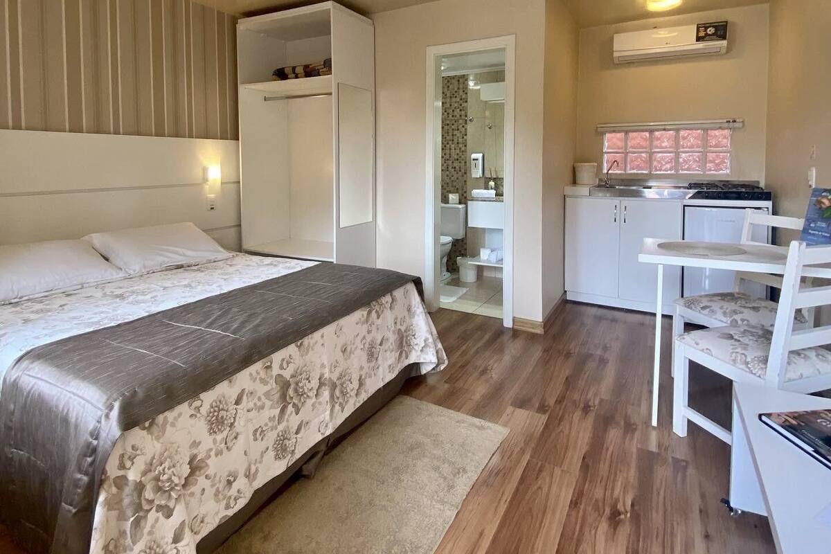 A bedroom with a bed, a desk, and a kitchenette.