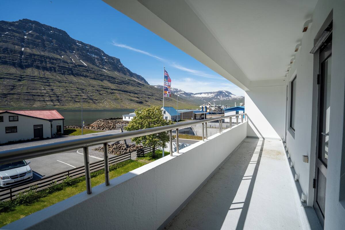 Een balkon met uitzicht op een berg, een vlag en een gebouw met een rood dak.