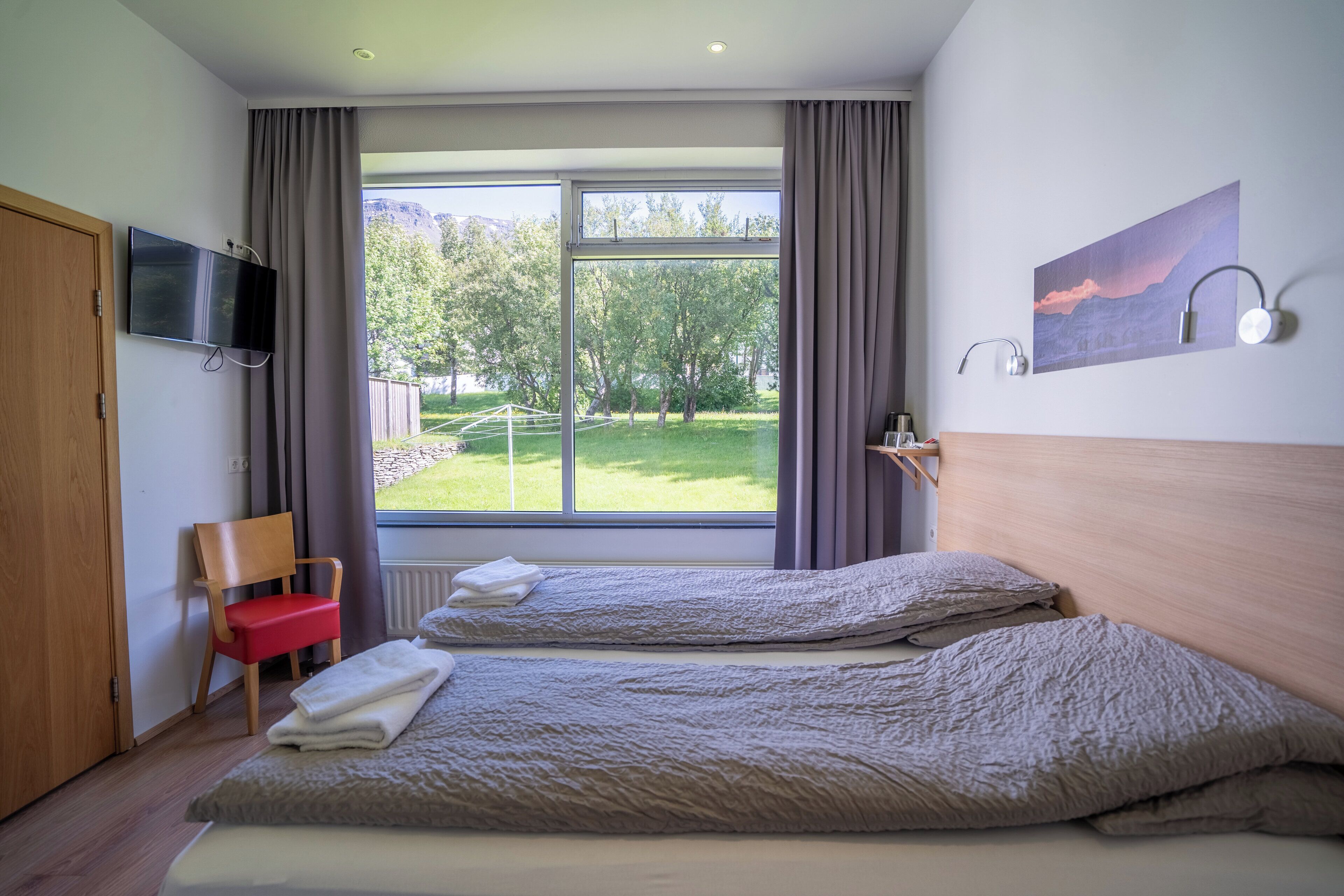 Habitación de hotel con dos camas, un televisor, un cuadro y vistas a un paisaje verde.