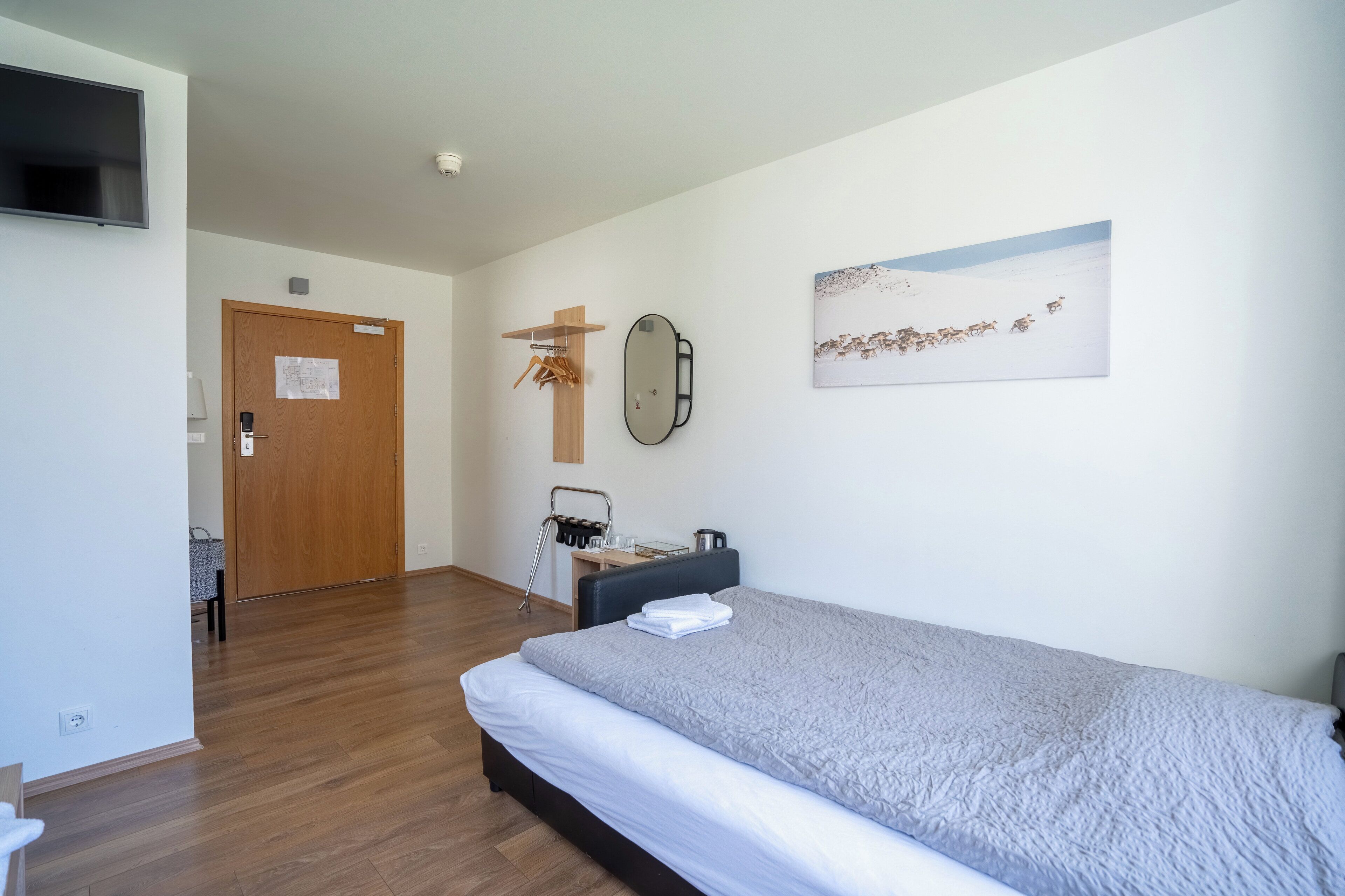 Une chambre d’hôtel avec un lit, un bureau, une chaise, une télévision, une porte et un tableau au mur.