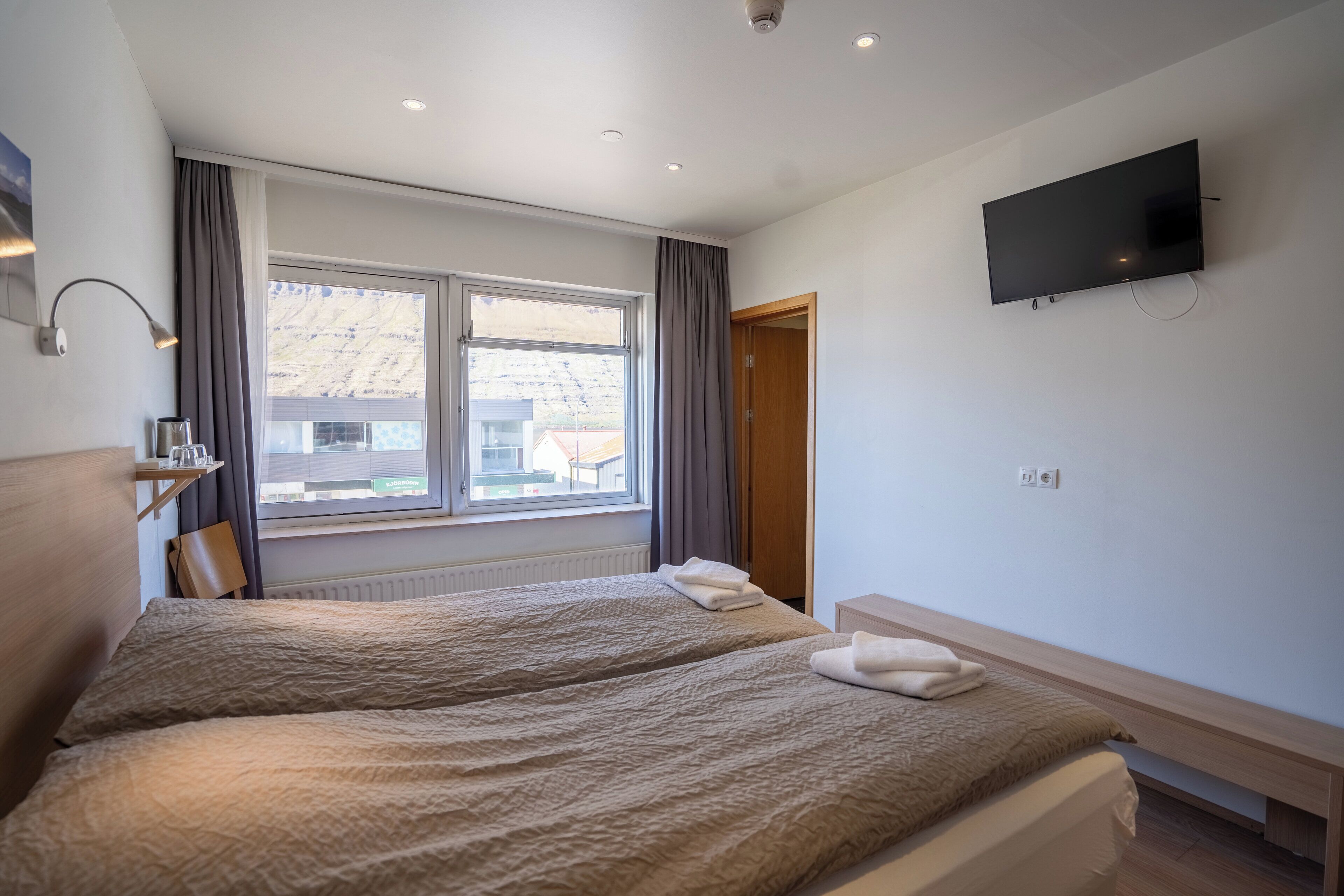 Habitación de hotel con dos camas, un televisor montado en la pared, una ventana con cortinas y un radiador.