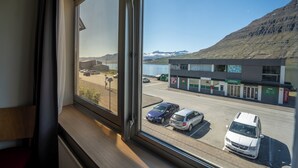 Uitzicht vanuit een hotelkamer op een parkeerplaats met verschillende auto's, een gebouw met een bordje en een berg op de achtergrond.