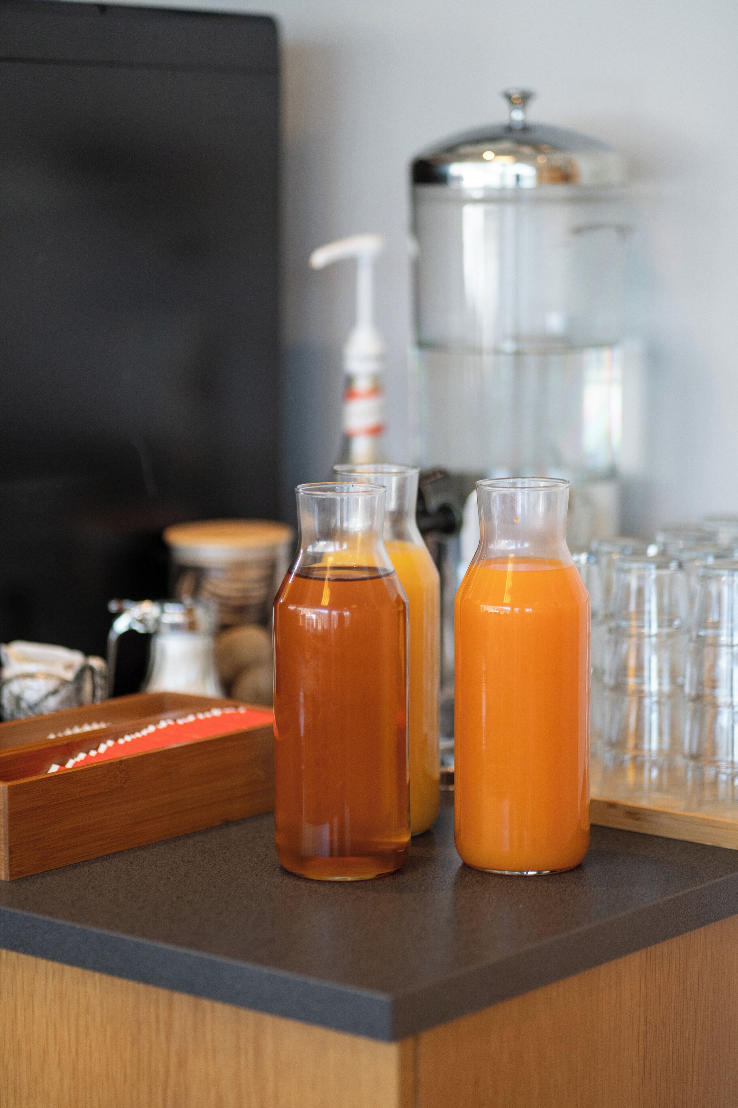 A bar area with several glass bottles of orange liquid, a water dispenser, and stacked glasses.