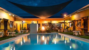 Une piscine dotée d’un patio couvert, d’un espace salon extérieur et d’un foyer central.