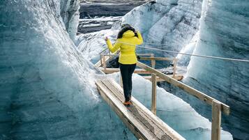 A person in a yellow jacket walking on a wooden bridge over a glacier.