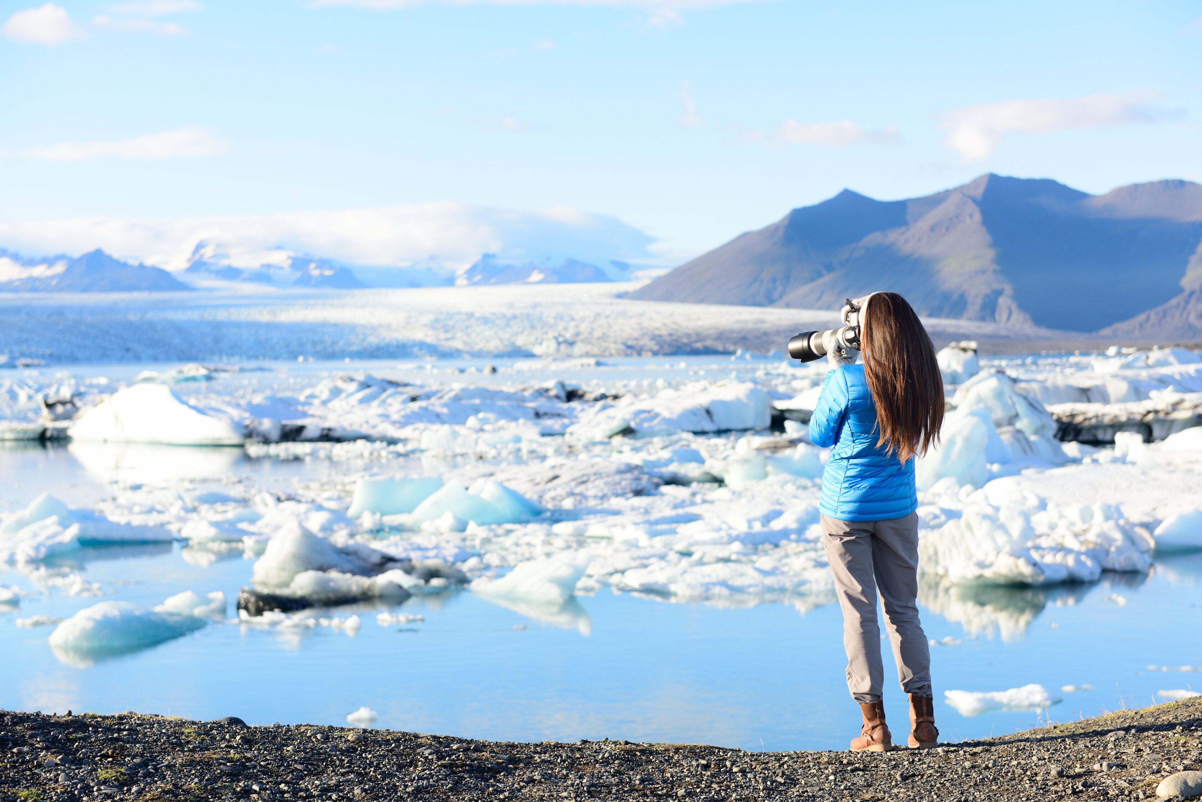 Una persona fotografiando un glaciar con montañas al fondo.