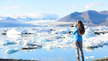 Una persona fotografiando un glaciar con montañas al fondo.