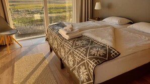 A hotel room with a large bed, a view of the countryside, a chair, and a lamp.