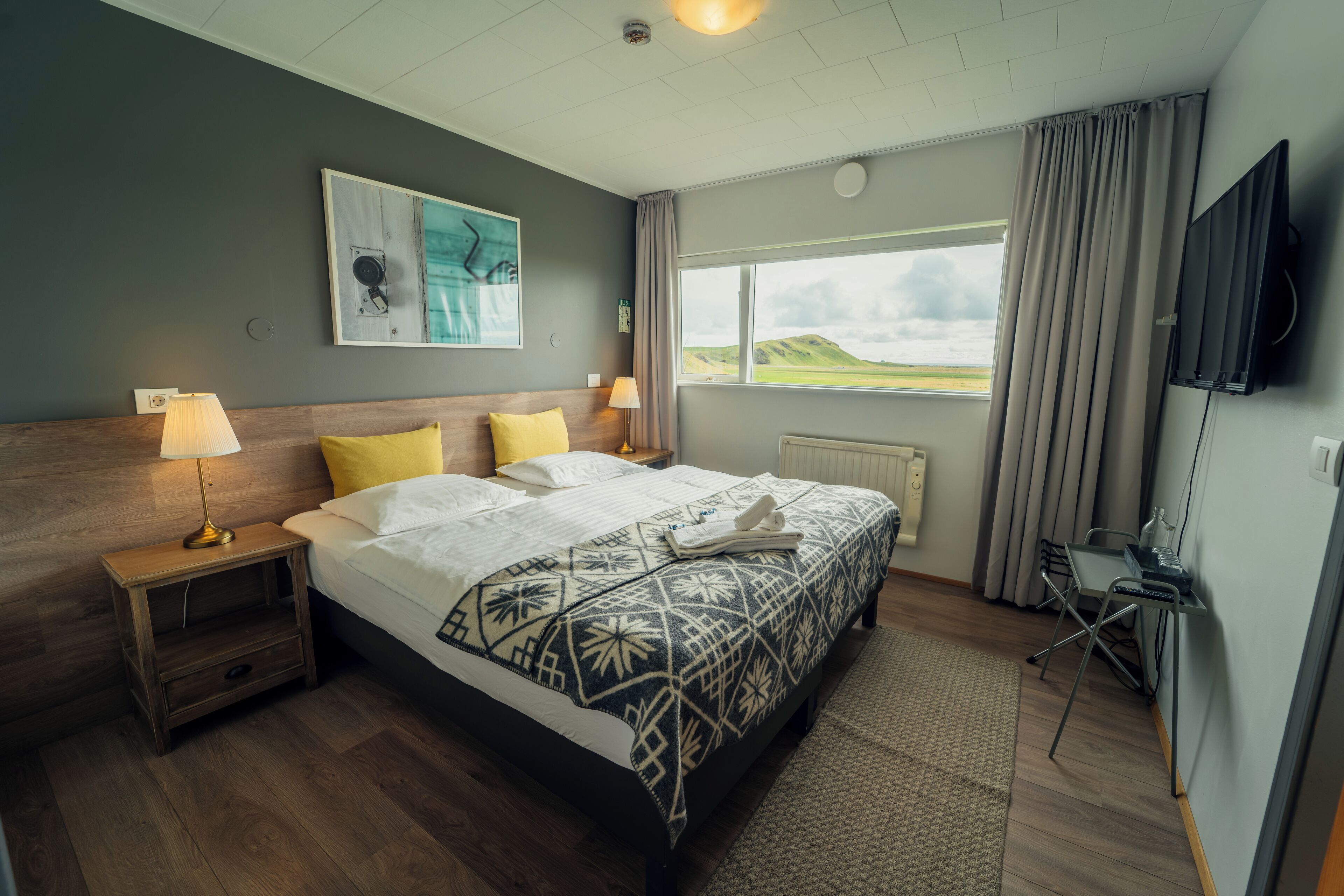 Ein Hotelzimmer mit Bett, Schreibtisch, Fernseher, Fenster mit Blick und einem Gemälde an der Wand.