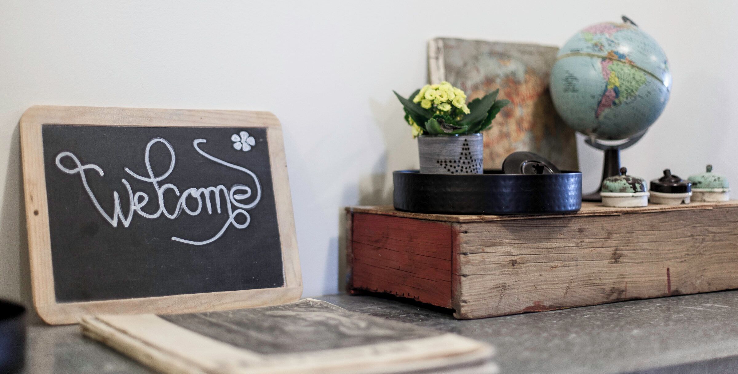 A welcome sign on a chalkboard, a globe, and a small potted plant on a wooden table.