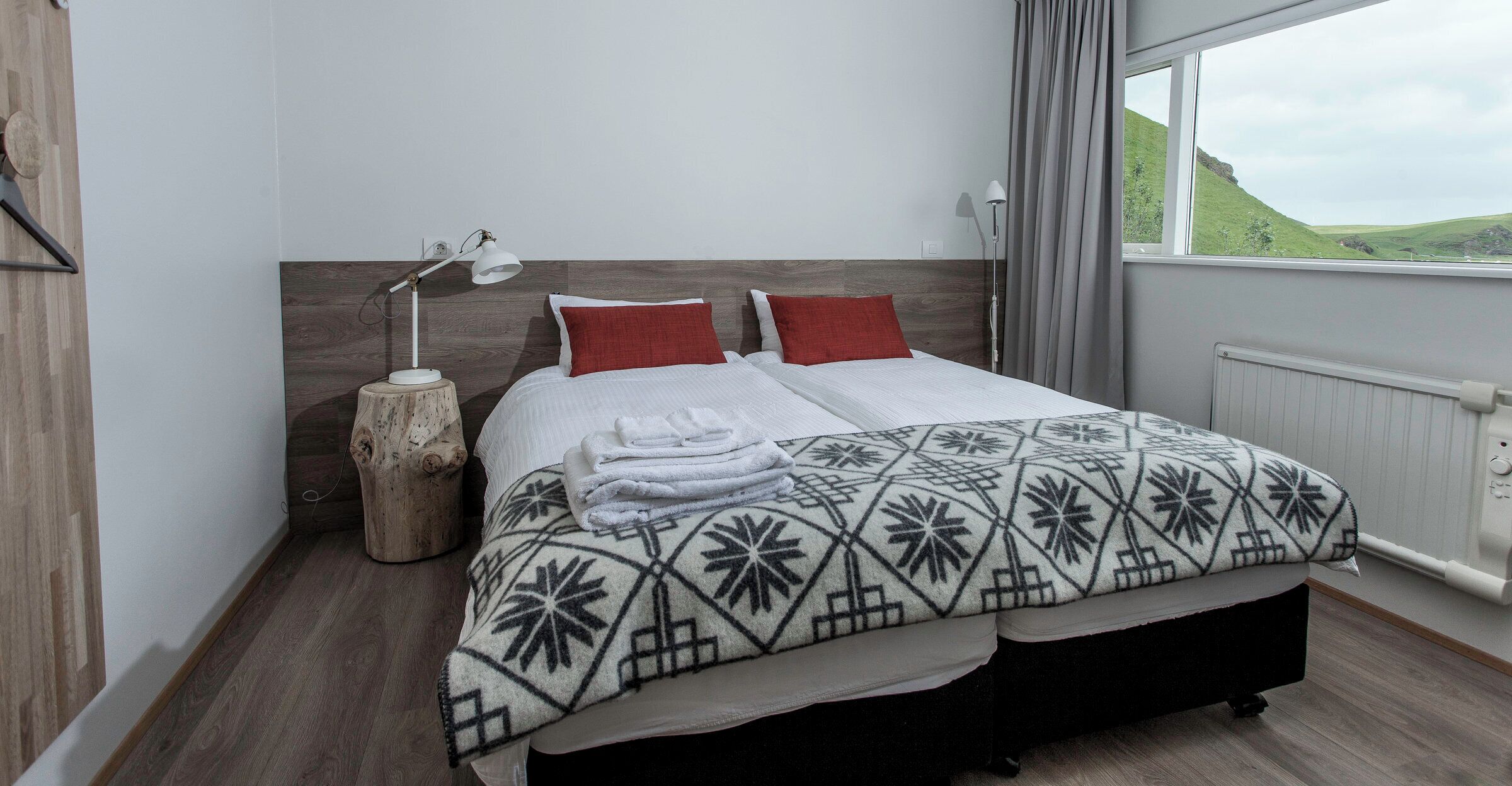 Una cama bien hecha con un edredón estampado, dos almohadas rojas y una lámpara de noche.