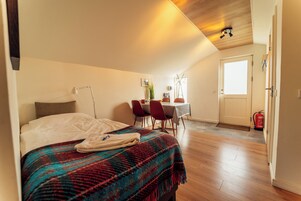 A bedroom with a bed, a bedside table, a chair, a small table, and a door.