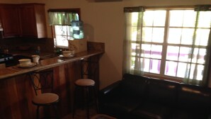 Eine Küche mit Holzausstattung, einer Bar mit Hockern, einem Glastisch und einem Fenster mit Jalousien.