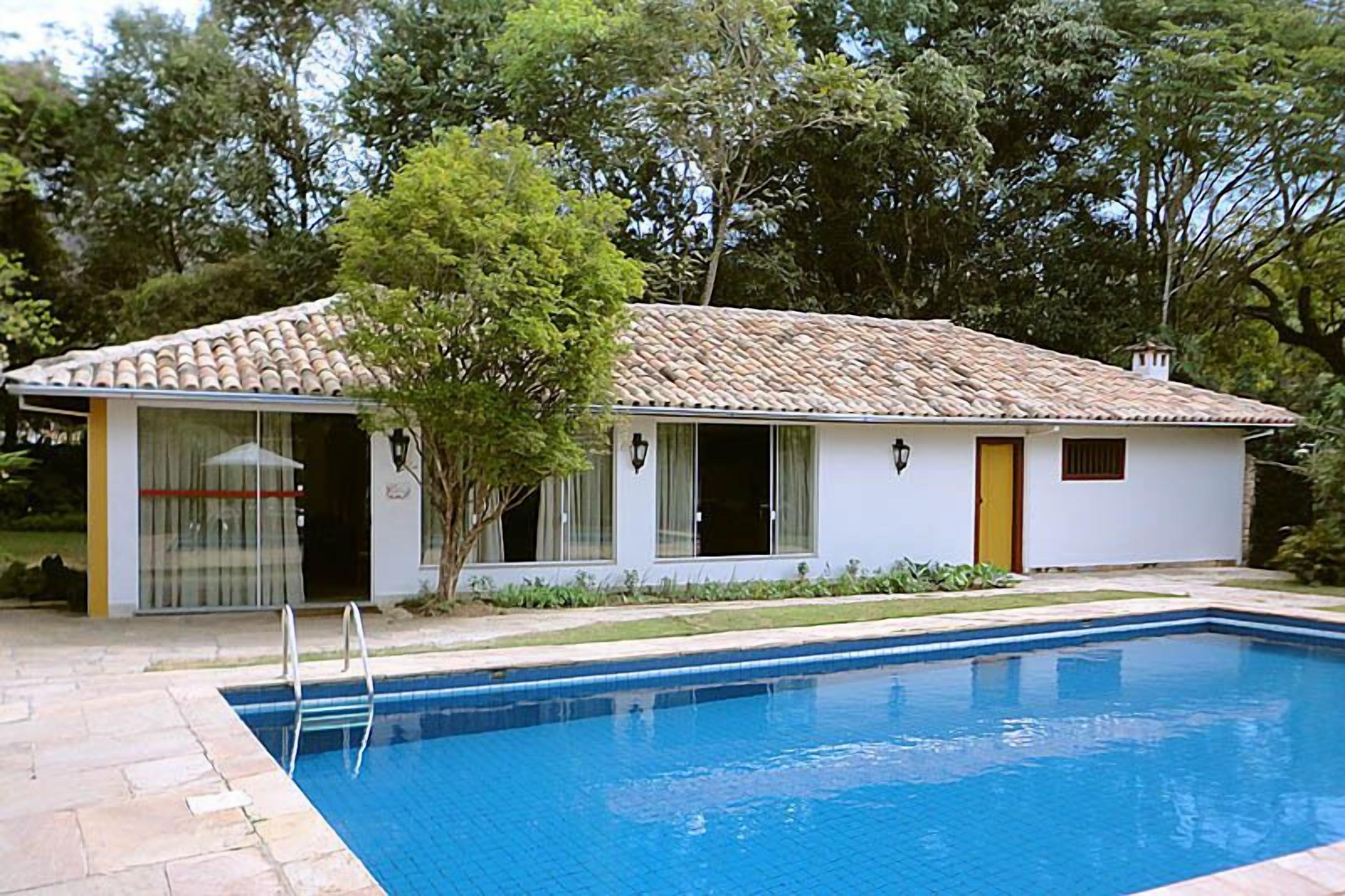 Uma casa térrea com telhado de telhas, piscina e um pequeno jardim.