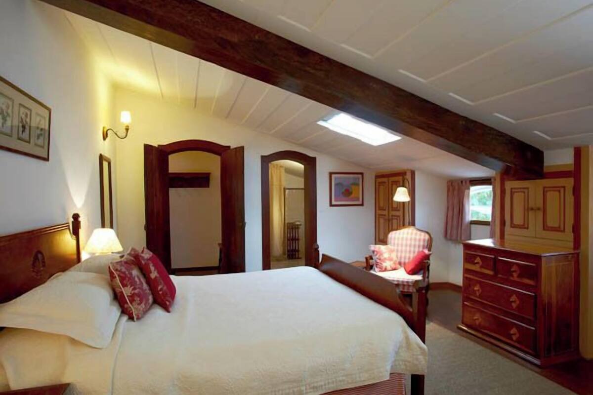 A bedroom with a large bed, wooden headboard, a dresser, and a chair.