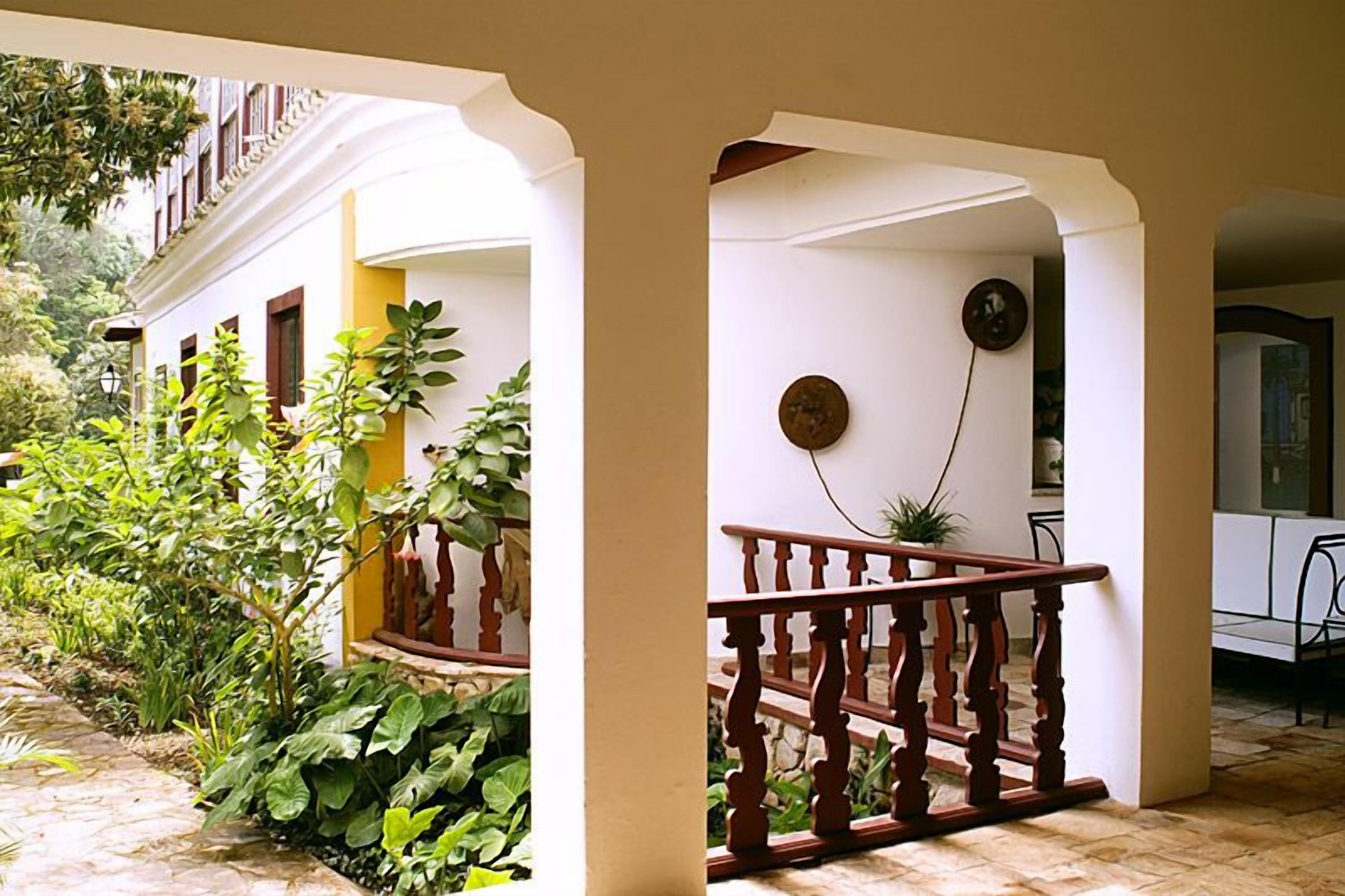 A covered outdoor area with a wooden railing, potted plants, and a stone floor.