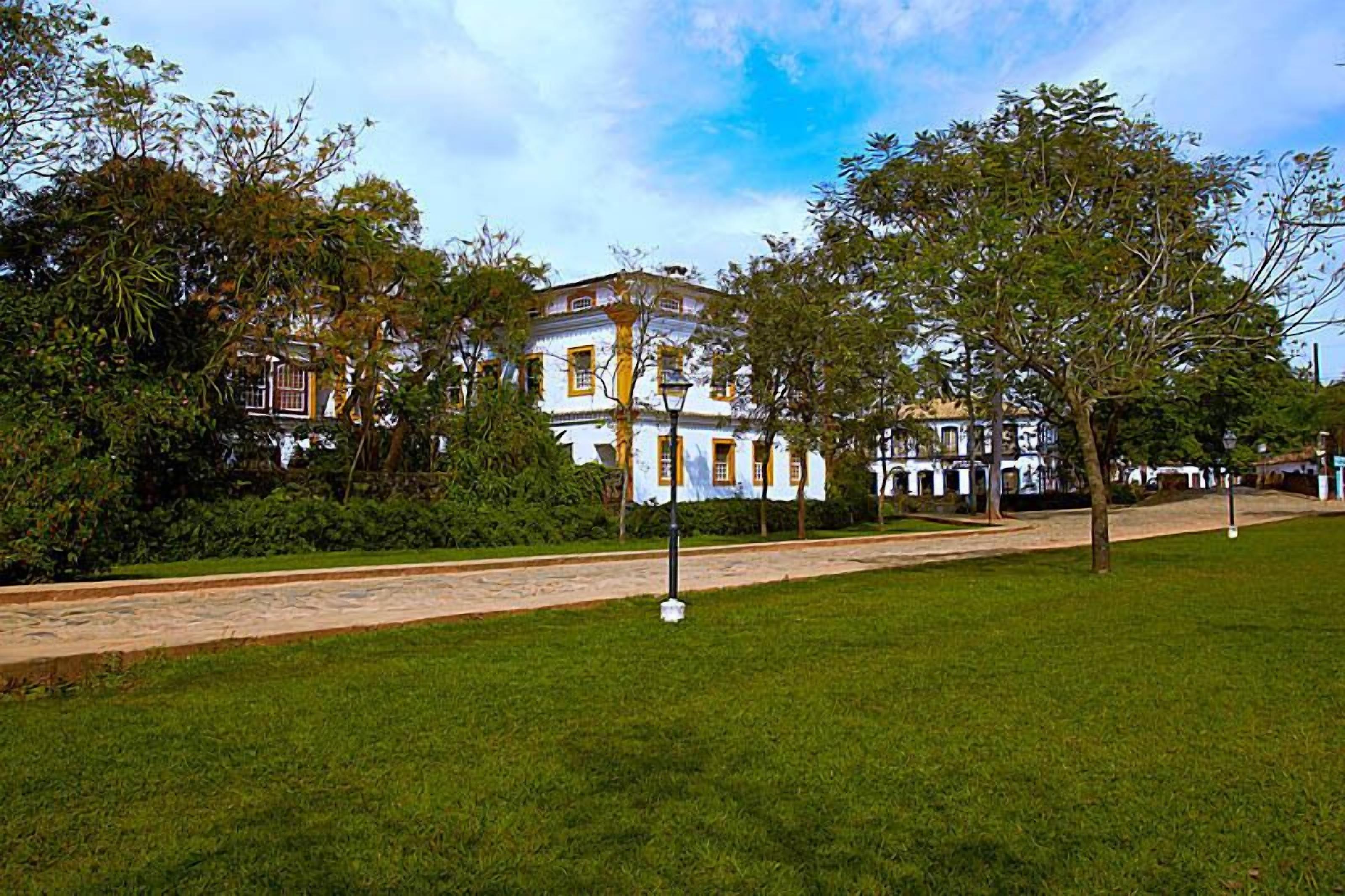 Un edificio con fachada blanca y detalles amarillos, rodeado de un césped cuidado y árboles.