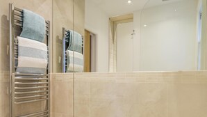 Ein modernes Badezimmer mit Duschkabine aus Glas, einem Handtuchhalter mit gefalteten Handtüchern und einem gefliesten Boden.