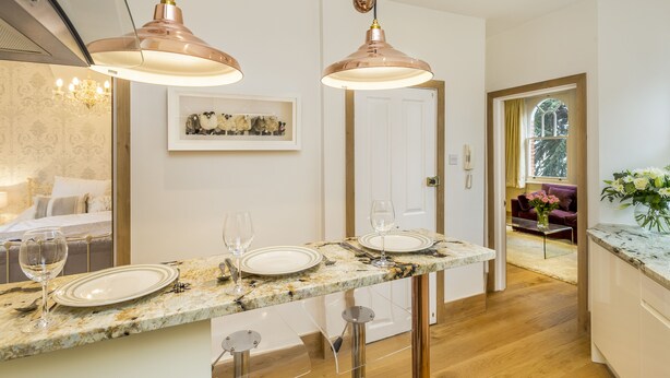 Eine moderne Küche mit Marmorarbeitsplatte, Pendelleuchten und einem Essbereich mit einer Couch und einem Blumenvasen.