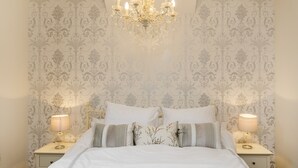 Ein Schlafzimmer mit einem großen Bett, zwei Nachttischen mit Lampen, einer Kandelaber und Wandtapete mit Muster.