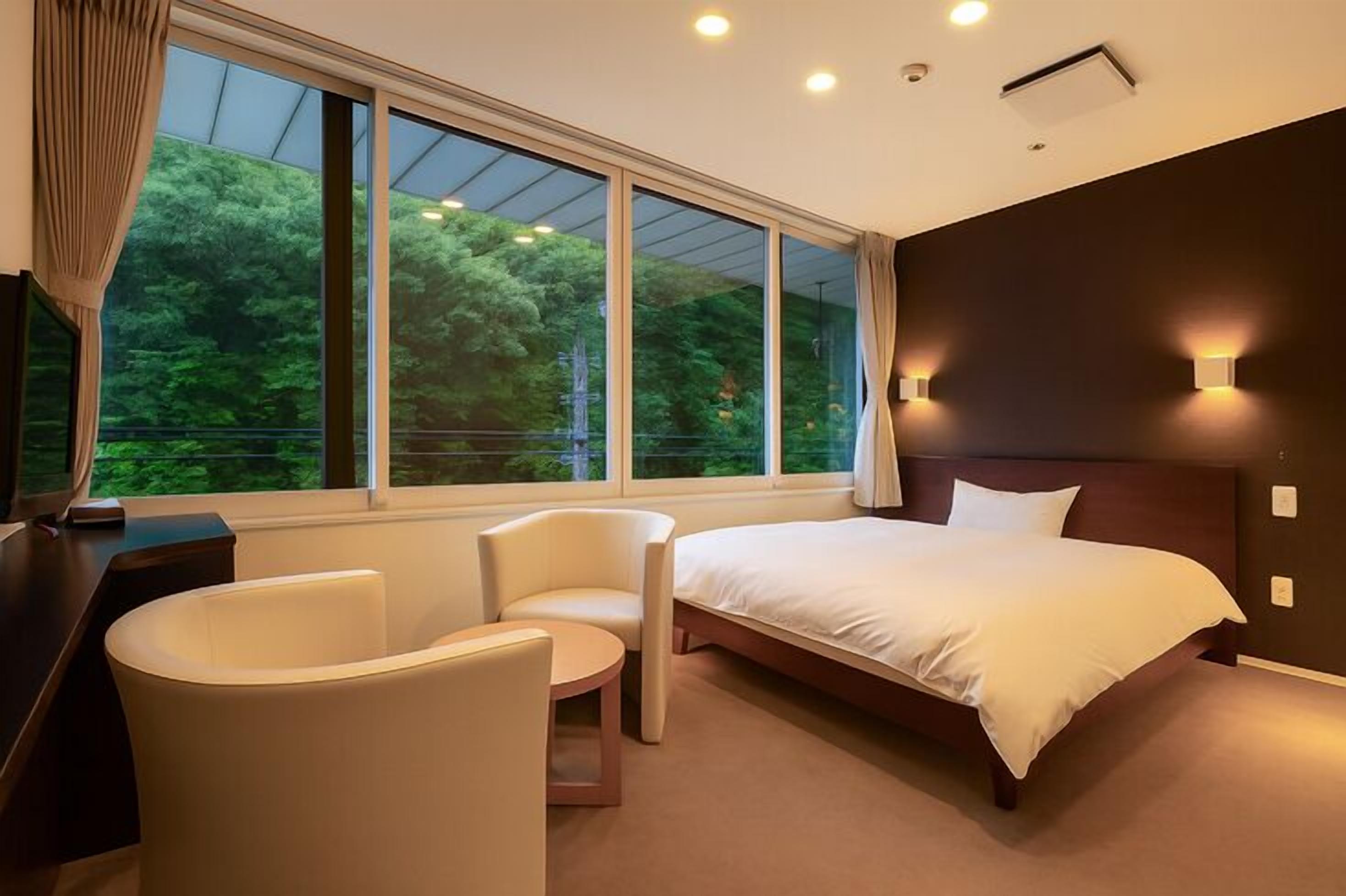 A hotel room with a large window, a bed, a desk, and a chair.