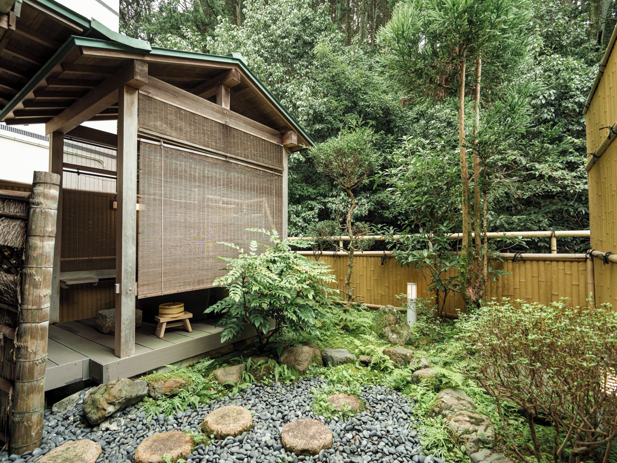 A traditional Japanese-style building with a wooden structure, a tatami mat entrance, and a garden with rocks and greenery.