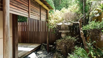 A wooden structure with a sloped roof, surrounded by a garden with rocks, plants, and a stone water feature.