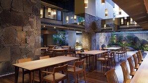 A restaurant with wooden tables and chairs, stone walls, and hanging pendant lights.