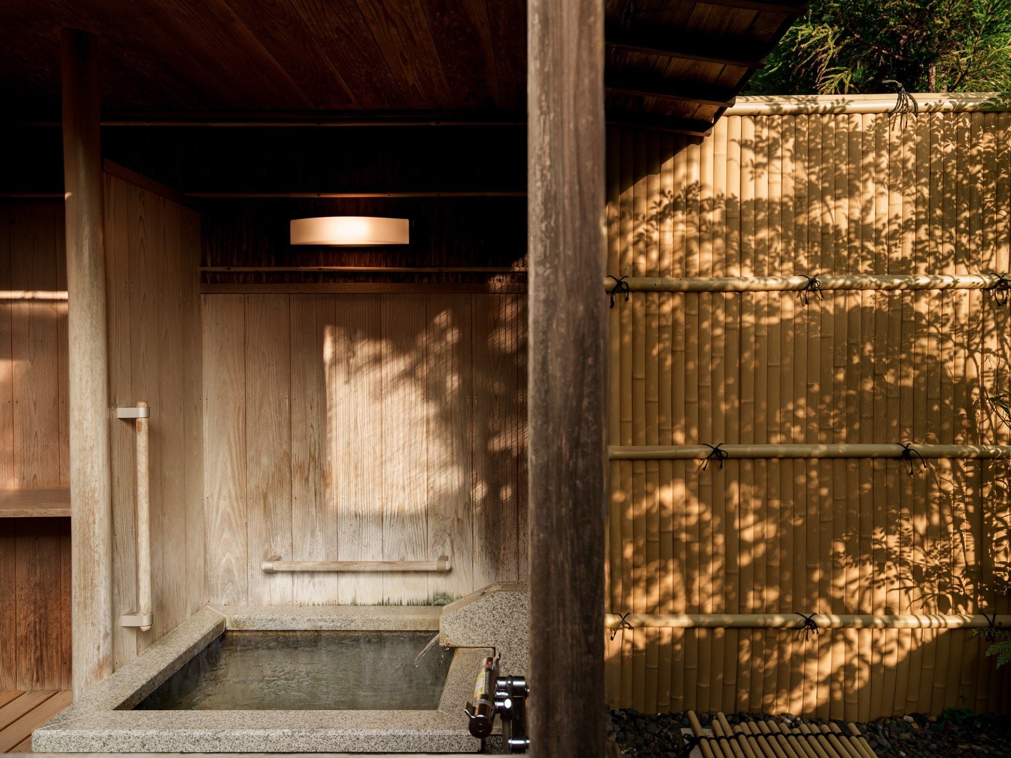 A traditional Japanese onsen with a wooden interior, a stone hot spring, and a bamboo fence.