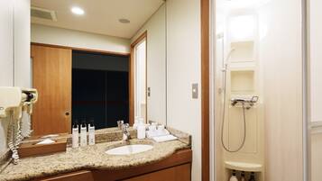 Baño de hotel con encimera de granito, dos lavamanos, un espejo y zona de ducha.