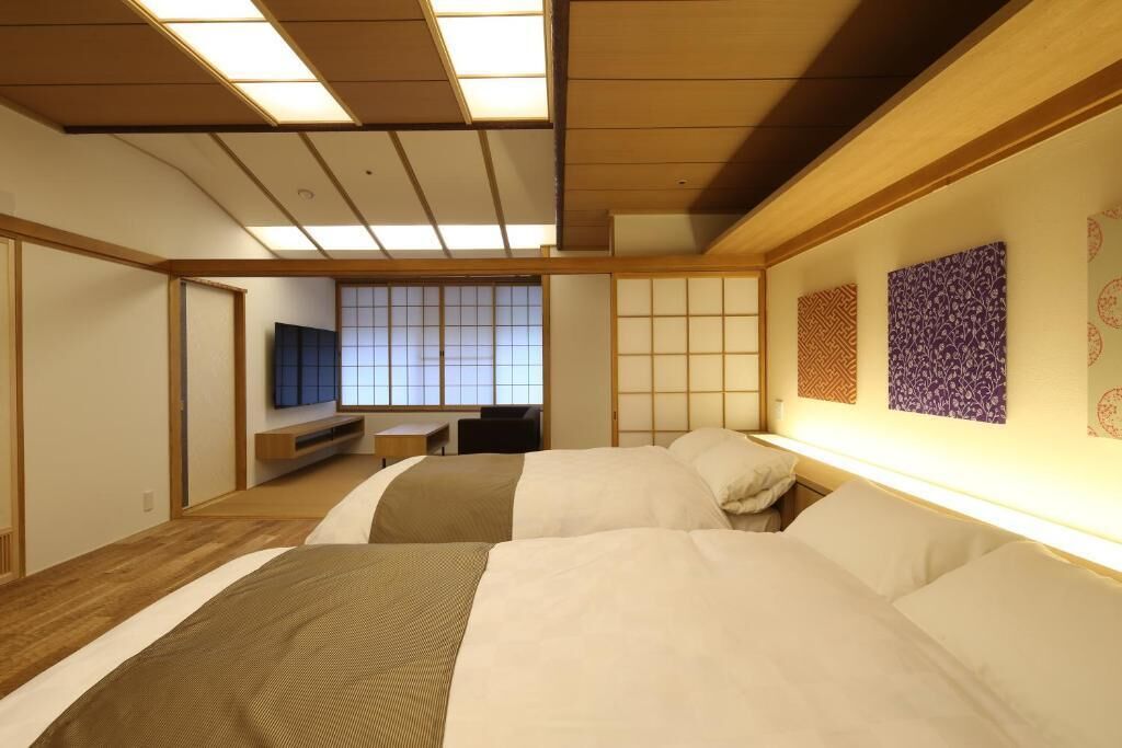 A traditional Japanese-style hotel room with tatami flooring, a low bed, a television, and sliding doors.