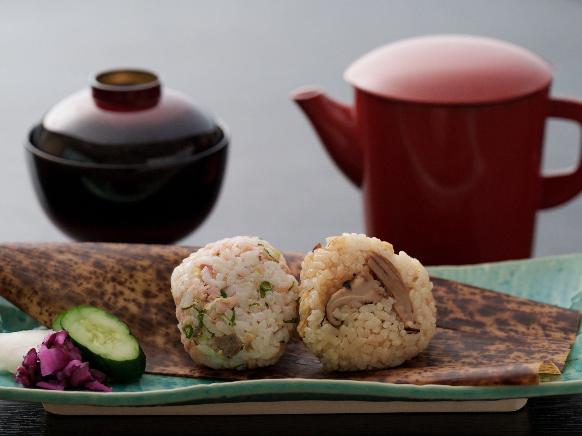 Una comida tradicional japonesa con onigiri de arroz, una rodaja de pepino y jengibre encurtido morado sobre un plato de madera.