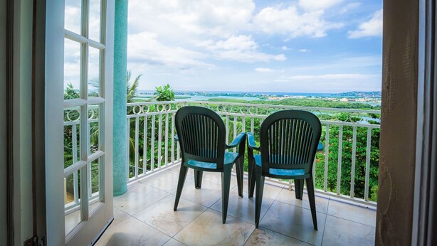 Un balcon avec deux chaises et une table, offrant une vue panoramique sur un paysage verdoyant et sur une ville située au loin.