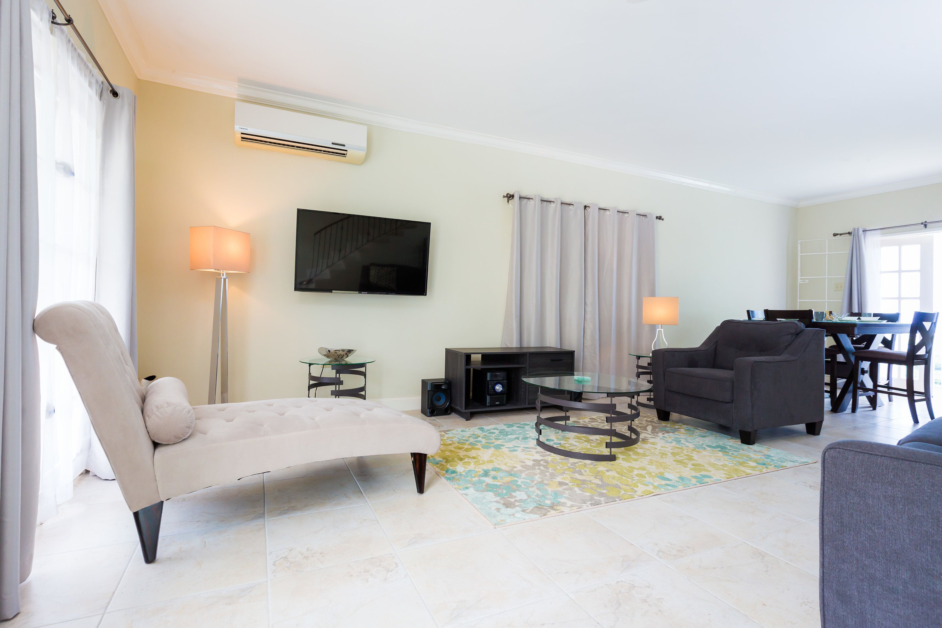 A modern living room with a sofa, armchair, and a dining area with a table and chairs.