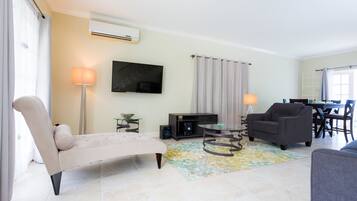 A modern living room with a sofa, armchair, and a dining area with a table and chairs.