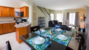 Une cuisine moderne avec des meubles en bois, un coin repas avec une table en verre pour quatre personnes, et un escalier menant à un autre niveau.