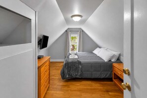 A bedroom with a bed, wooden dresser, and a television on the wall.