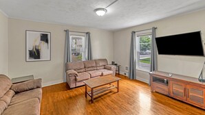 Een woonkamer met een beige bank, een houten salontafel, een flatscreen televisie en een kast.