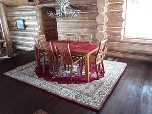 Uma mesa de jantar de madeira com seis cadeiras, cercada por um tapete estampado, em um interior de cabana rústica.