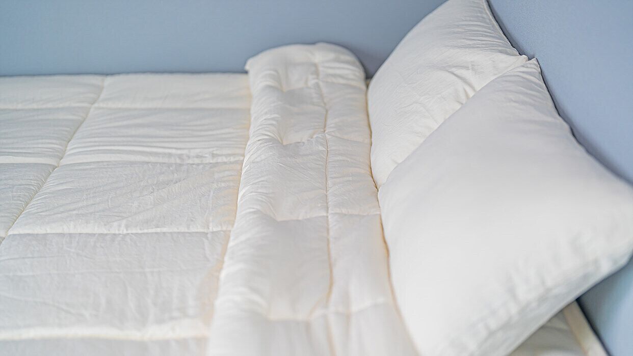 A bed with a white mattress and pillows against a light blue wall.