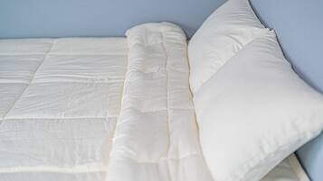 A bed with a white mattress and pillows against a light blue wall.