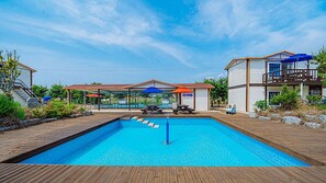 A swimming pool with a wooden deck, lounge chairs, and umbrellas. - Wando Sol Beach Pension (Wando)