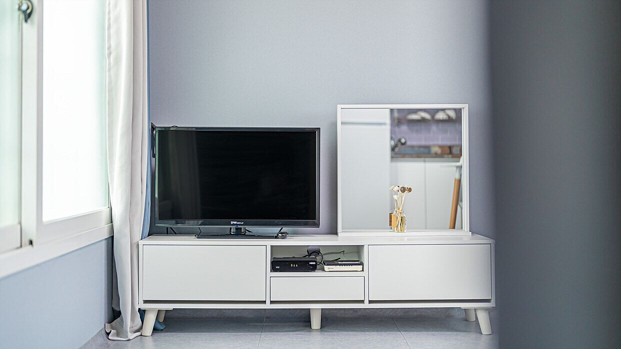Et moderne, hvidt tv-møbel med et fladskærms-tv, en lille skabsdel og en dekorativ vase.