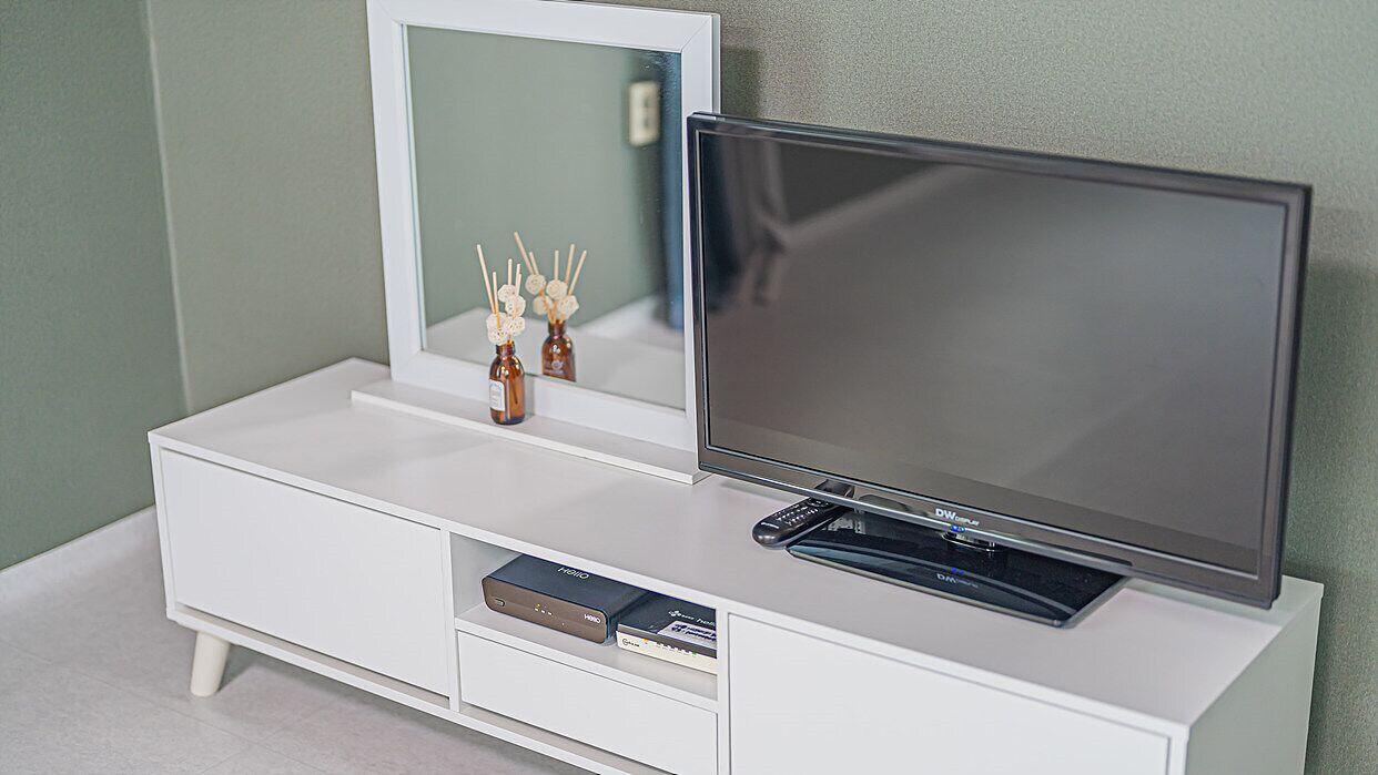 Un mueble blanco de entretenimiento con un televisor de pantalla plana, un espejo y un estante pequeño con objetos decorativos.