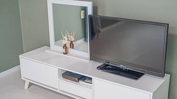Un mueble blanco de entretenimiento con un televisor de pantalla plana, un espejo y un estante pequeño con objetos decorativos.