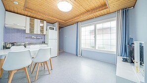 A modern kitchen with white cabinets, a microwave, and a sink. There are three white chairs around the table. - Wando Sol Beach Pension (Wando)